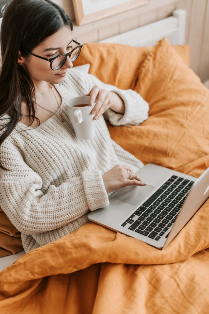 Henrike hilft - Technik ohne Stolperfallen - Frau mit Laptop auf Schoß entspannt im Bett mit Tasse Kaffee in der Hand